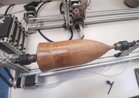 The bare wooden mandrel of the nose cone, mounted between the chucks of the four-axis XWinder machine on its aluminium profile frame.